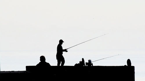 The fascinating silhouette of amateur fishermen on the rocks against the sky