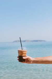 Cropped hand holding coffee against sea