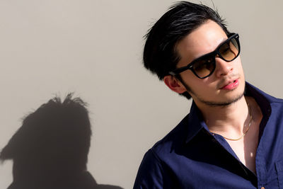 Portrait of young man wearing eyeglasses standing against wall