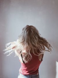 Rear view of woman with tousled blond hair against white wall