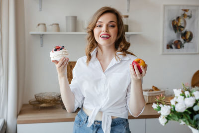 Girl holding a cake in one hand and an apple in the other in the kitchen