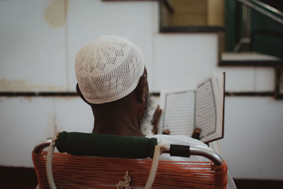 Rear view of a man with gray beard reading the quran in a mosque 