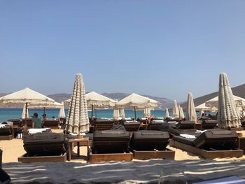 Lounge chairs and parasol arranged at beach against clear sky