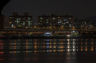 Wet road by illuminated buildings in city at night