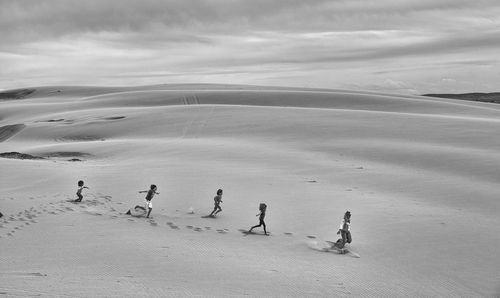 High angle view of people running in desert against cloudy sky