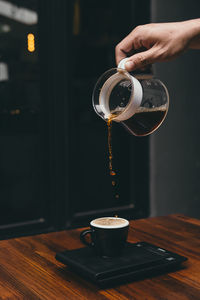 Cropped hand of person pouring coffee in cup on table