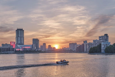 Sea by buildings against sky during sunset