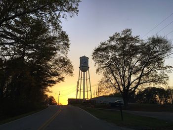 Silhouette trees on road against sky at sunset