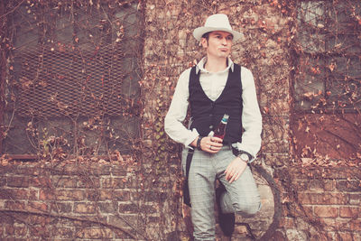 Man holding bear bottle while standing against wall