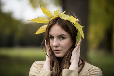 Close-up portrait of beautiful young woman holding leaf crown