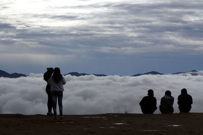 Rear view of people standing on land against sky