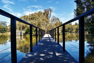 Footbridge amidst plants and trees against sky