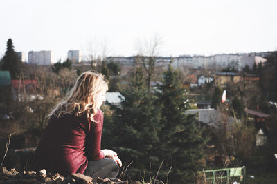 Woman sitting in city against sky