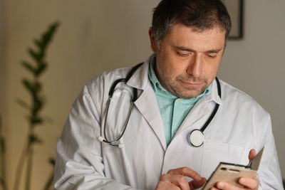 Close-up of smiling mature man using smart phone against wall