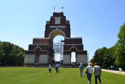 People walking in front of historical building against clear sky
