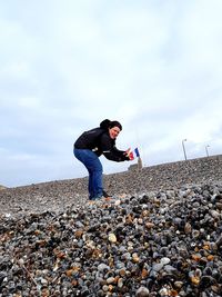 Side view of young woman standing on rock against sky