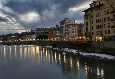 River by illuminated buildings against sky at dusk