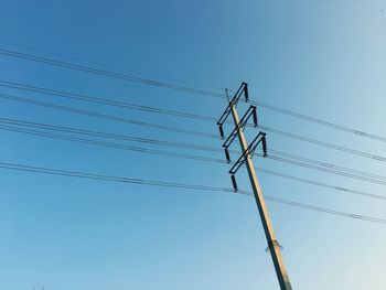 Low angle view of electricity pylon against clear blue sky