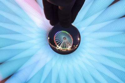 Cropped hand holding crystal ball with reflection of illuminated ferris wheel at night