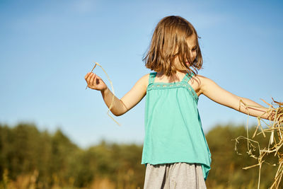 Cute little girl sits on mown rye in the field in summer