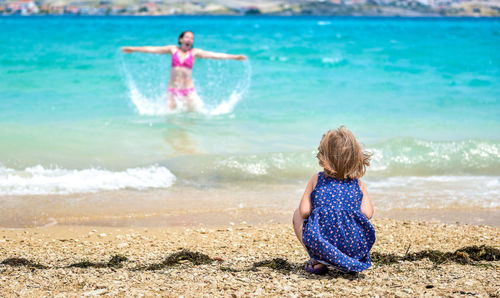 Rear view of daughter looking at mother enjoying in sea