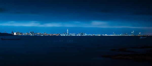 Illuminated city by sea against blue sky