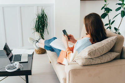 Business woman sitting on the couch works with documents counting on a calculator on a mobile phone.