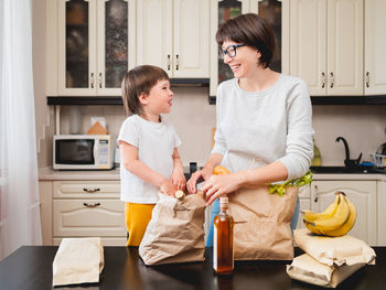 Woman and toddler boy sort out purchases. grocery delivery in paper bags. mother and son at kitchen.