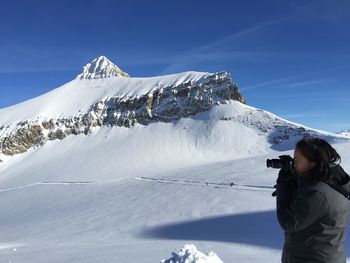 Woman photographing snowcapped mountains against sky