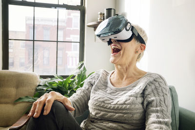 Senior woman wearing virtual reality simulator while sitting on sofa