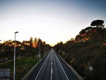 Road by trees against sky during sunset