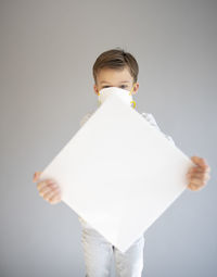 Portrait of cute boy wearing mask standing against gray background