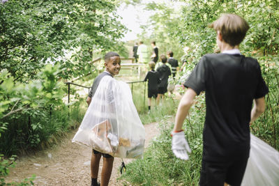 Smiling teenage boy looking back while carrying garbage bag