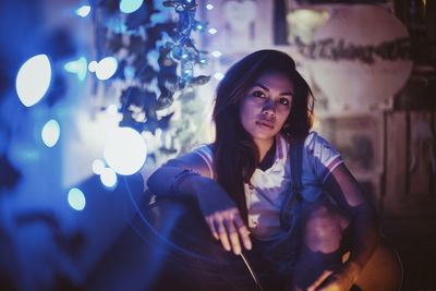 Portrait of young woman sitting in illuminated nightclub