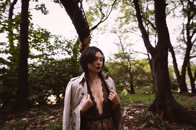 Young woman standing by tree in forest