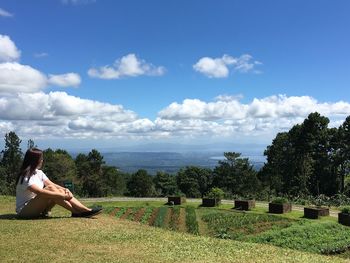 Woman sitting on grassy field against sky