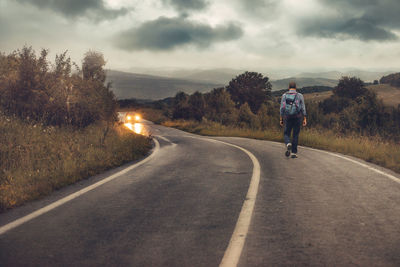 Rear view of man walking on road against sky