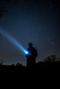 Silhouette young man holding flashlight while standing on field against star field at night