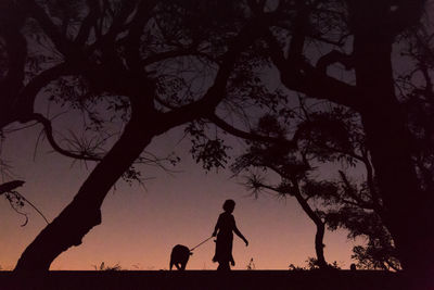 Silhouette woman with dog against sky during sunset