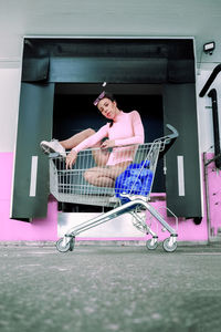 Full length portrait of woman sitting in shopping cart