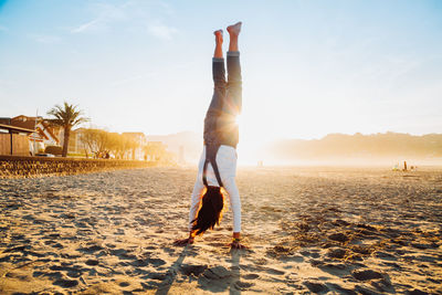 Rear view of woman walking on beach against sky during sunny day