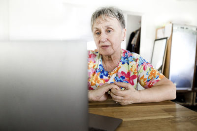 Senior woman sitting at table at home using laptop