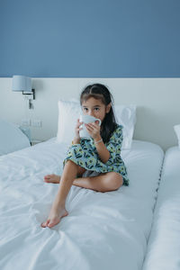 Cute little girl drinking milk on bed