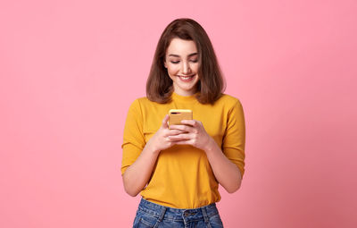Smiling young woman using mobile phone against red background