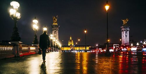 Rear view of man walking on pont alexandre iii leading towards hotel des invalides at night