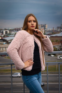 Beautiful young woman standing on railing against cityscape