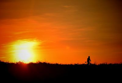 Silhouette man riding bicycle on field against orange sky