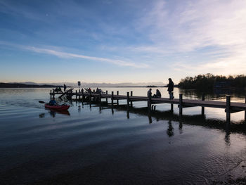 Silhouette people on pier over lake against sky during sunset