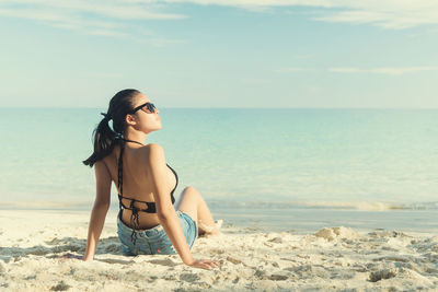 Rear view of young woman relaxing on sandy beach