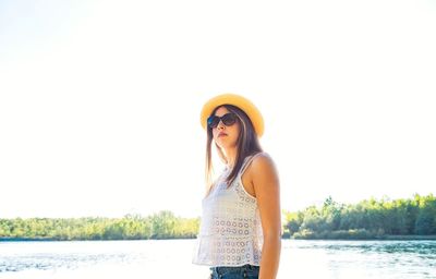 Portrait of smiling young woman standing by lake against clear sky